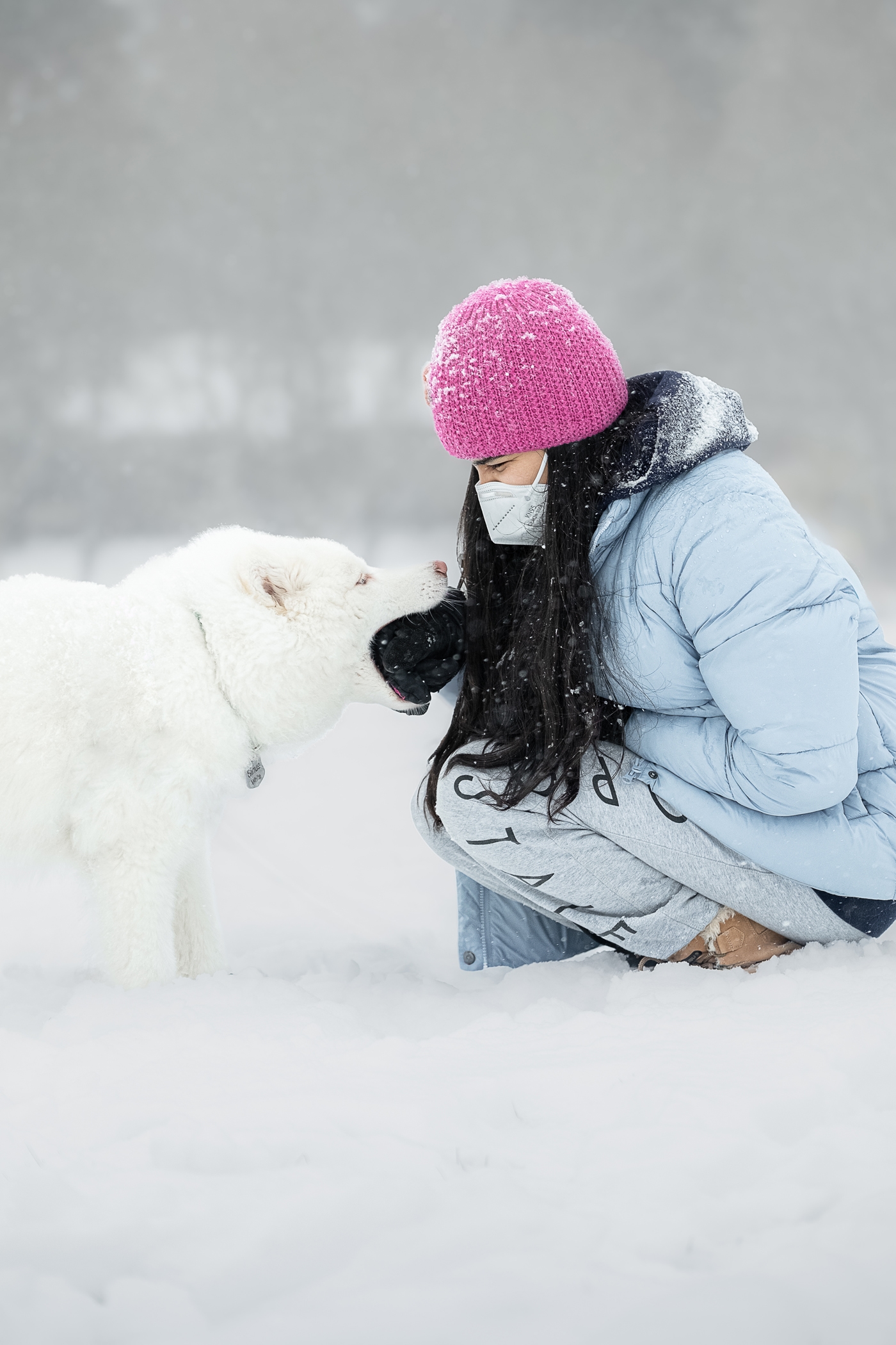 Woman in winter attire playing with a white dog in the snow.