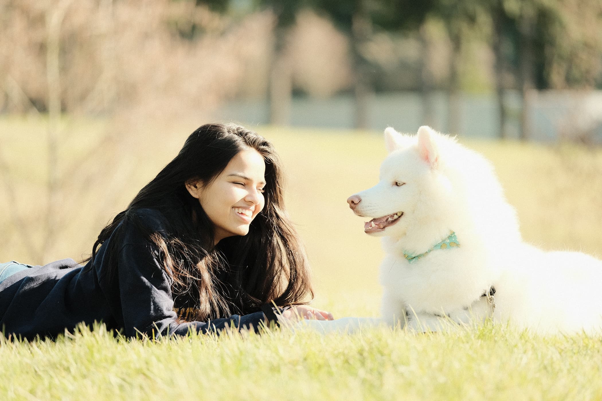 Snuggly Snouts about photo young woman smiling at a fluffy white dog in a sunny park setting.